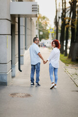 Fototapeta na wymiar Cute European middle-aged couple holding hands walking in the city street, man and woman walking down the street in summer, back view