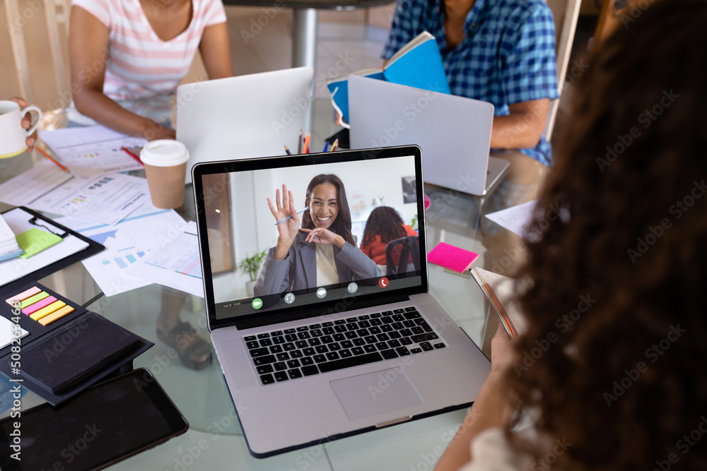 Poster Smiling african american businesswoman waving hand to biracial female colleague on video call