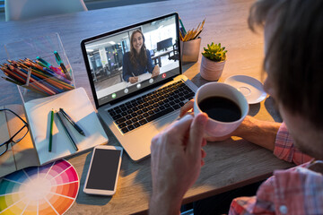 Caucasian businessman having coffee during video call with female caucasian colleague