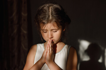 Fototapeta na wymiar A little girl folded her hands in prayer in the hope of ending the war in Ukraine, a Ukrainian child prays and believes in a happy future