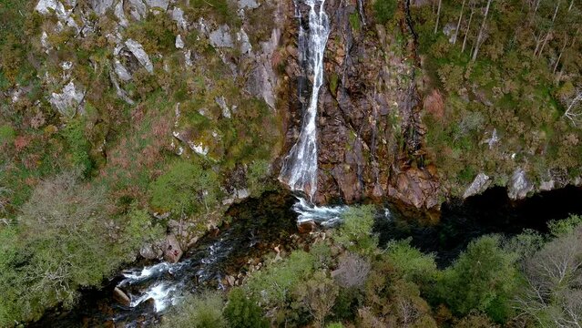 Waterfall falls into the Sor River by the cliff surrounded by forests and people taking pictures by the river. Overhead drone shot blocked. Mirador Aguas Caidas, Lugo, Galicia, Spain