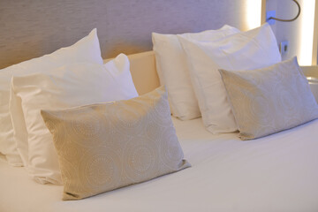 A lot of pillows are placed on a bed inside a hotel room. White sheets on the matrimonial bed.