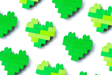 Obraz premium Green hearts from blocks isolated on white background, minimal geometric pattern from plastic blocks, shapes heart from child construction. Top view pattern, Toys and games.