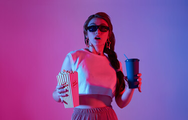Young woman wearing 3D glasses holding popcorn and beverage watching exciting movie isolated on...