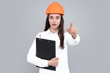 Architect woman in helmet pointing on copy space. Young woman in helmet hold clipboard on gray background. Female worker in hardhat helmet pointing to you.