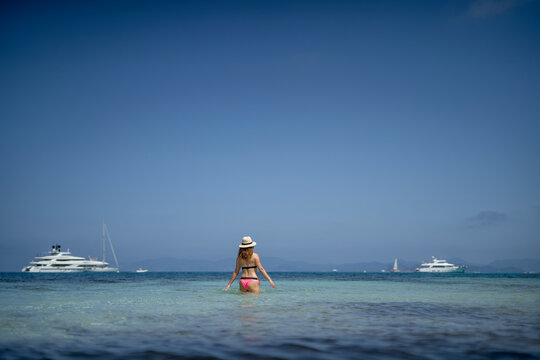 A woman with a hat walking in the paradisiacal sea in Formentera Spain