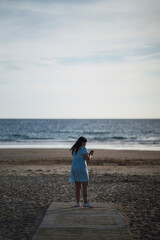 mujer de espaldas tomando fotos en la playa sobre camino de madera 