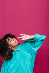 african american woman in blue blouse posing with hand near face and looking up isolated on pink.
