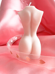 candle in the shape of a body, standing with its back. around the body is a beautiful ribbon with hearts.
