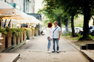 Fototapeta na wymiar Cute European middle-aged couple hold hands and walk through the streets of the city, near the cafe, summer walks and travel