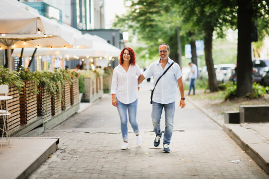 Fototapeta Cute European middle-aged couple hold hands and walk through the streets of the city, near the cafe, summer walks and travel