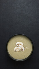 Top view of mushroom cream soup in black bowl with copy space. Slices of mushroom on the soup