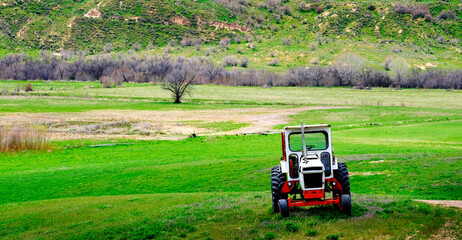 Fototapeta premium Old Tractor on Farm Field Green with Hills Mountains