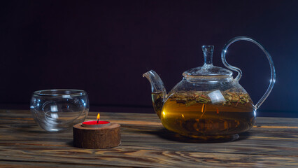 Hot herbal tea in glass teapot on wooden table on dark background. Traditional herbal drink. Place for text or design.