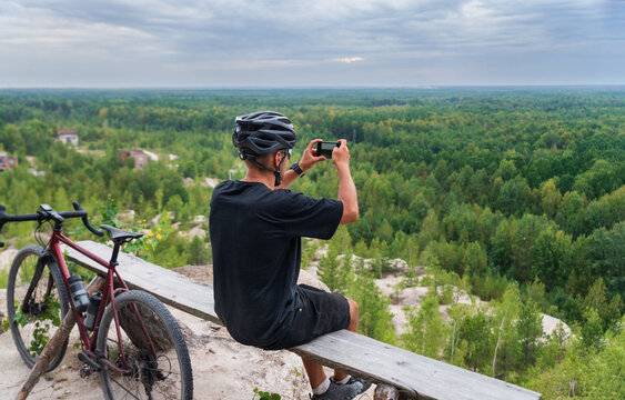 A cyclist takes pictures of a beautiful landscape on his mobile phone while training on a bicycle. Sport and travel.