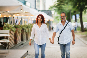 Cute European middle-aged couple hold hands and walk through the streets of the city,, summer walks...