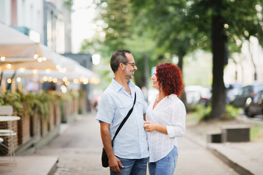 Fototapeta Cute European middle-aged couple hold hands and walk through the streets of the city,, summer walks and travel