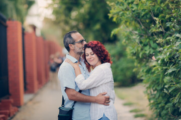 Obraz premium Cute European middle-aged couple hold hands and walk through the streets of the city,, summer walks and travel