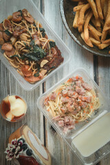 Take home meal on wooden table; Spagetti, french fries top view