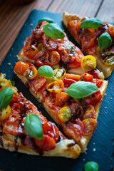 Close-up of tomato puff pastry tart with balsamic vinegar and fresh basil on stone plate