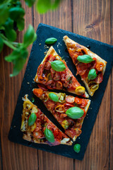 Tomato puff pastry tart with balsamic vinegar and fresh basil on stone plate, top view 