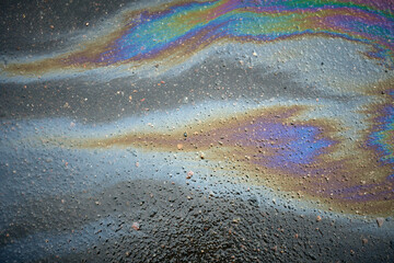 Oil stain on the asphalt, rainbow-shaped colored gasoline stains on an asphalt road as a texture or background
