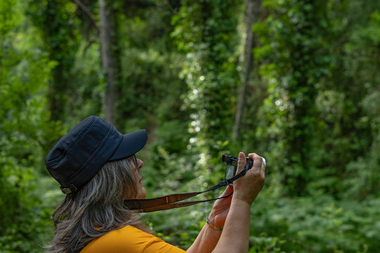 white-haired woman with cap taking photos in the forest