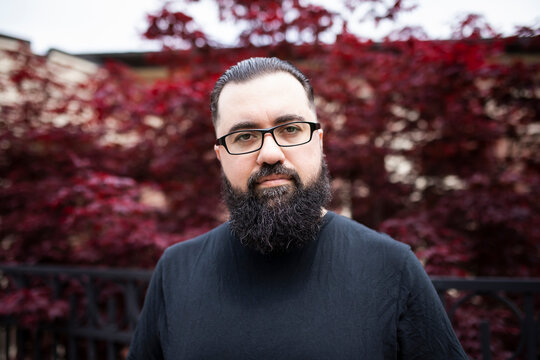 Headshot of a bearded man with glasses in front of a red maple tree