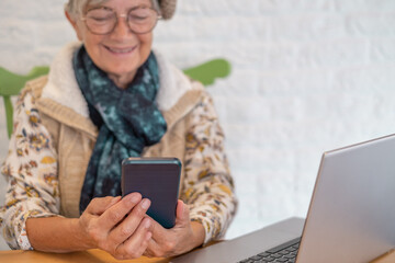 Beautiful caucasian senior woman reading text message on mobile phone while sitting with net-book in cafe, charming female using cell telephone and laptop computer during rest in coffee shop