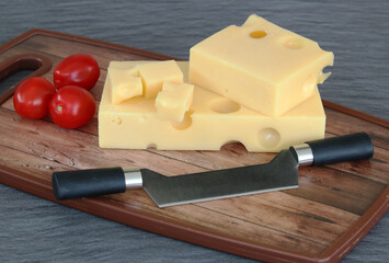 Emmentaler Käse mit Tomaten und Messer auf einem Holzbrett.