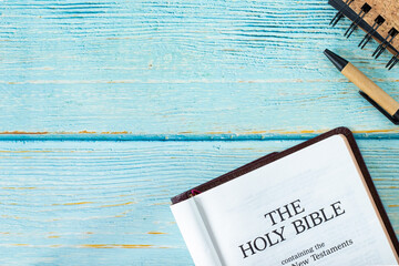 Open Holy Bible Book on a wooden table background with a pen and notebook. Copy space. Top view....