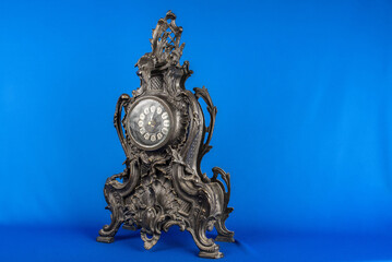 vintage bronze watch on a blue background, bronze fireplace clock, dark old desktop clock on a blue background, antique clock studio photo, antique table bronze clock on a blue background