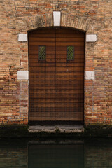 old brick wall and wooden door by a canal in Venice, Italy 