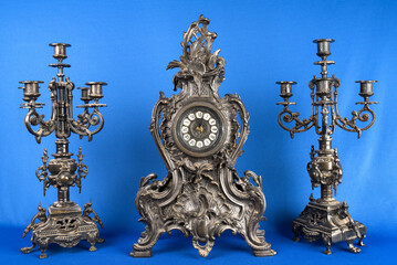 Antique table clock and two candlesticks. Vintage bronce watch with candelabra. Bronze clock and candelabra. Dark candlesticks and clock. Antique fireplace clock and candlesticks. 