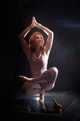 Obraz premium An adult skinny blonde woman doing yoga exercises on a black background in the studio. Sporty girl model posing in a photo shoot