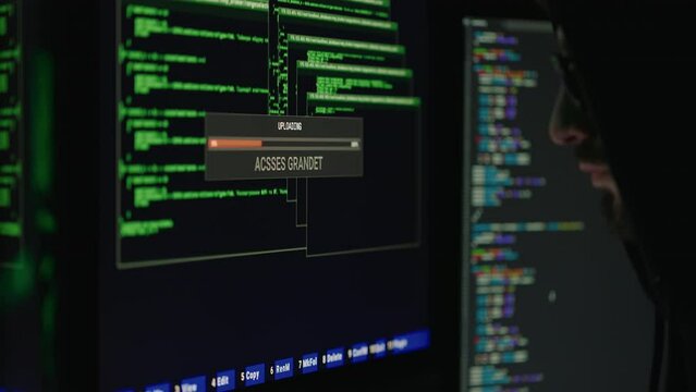 Dangerous hooded computer genius cracking database in dark room. Side view of cybercriminal getting unauthorized grandet access to personal banking data.