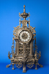vintage bronze watch on a blue background, bronze fireplace clock, dark old desktop clock on a blue...