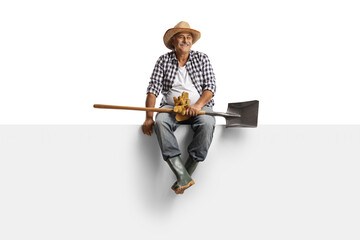 Full length portrait of a mature farmer with a spade sitting on a blank panel