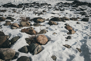 Gray cobblestones in frozen snow of winter steppe. Stones warmed up on warm day, opened from ice.