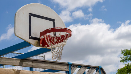 Naklejka premium Close-up of a basketball hoop, red, in the open air, the blue sky with fluffy clouds in the background.