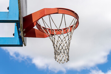 Naklejka premium Close-up of a basketball hoop, red, in the open air, the blue sky with fluffy clouds in the background.