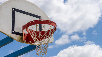 Close-up of a basketball hoop, red, in the open air, the blue sky with fluffy clouds in the...