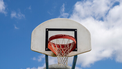 Close-up of a basketball hoop, red, in the open air, the blue sky with fluffy clouds in the...
