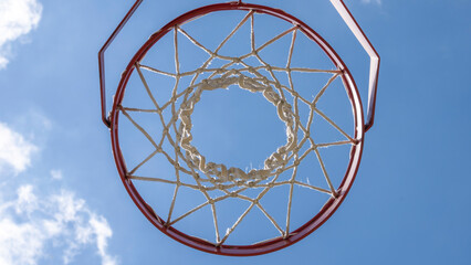 Close-up of a basketball hoop seen from below, blue sky in the background