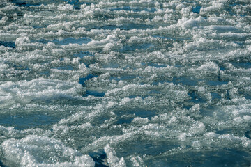 Round ice floes with fluffy edges in turquoise water of mountain river. Sunny frosty morning in surf zone. Dangerousness of movement and navigation. 