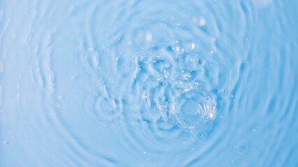 Naklejka na ściany i meble Drops fall down into clear fresh water on light blue background view from above