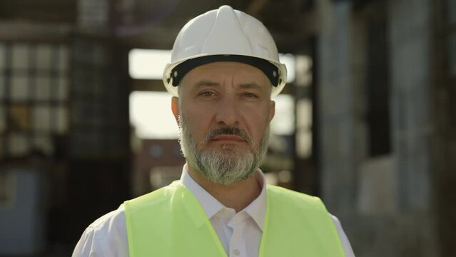 Portrait of caucasian male builder in reflective jacket looking at camera with calm face. Experienced senior man wearing helmet for preventing accident at work.