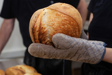 A baker in uniform holds freshly baked bread in his hands. Working mood.