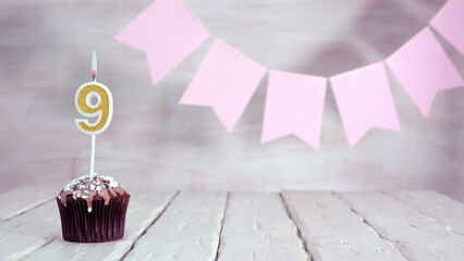 Birthday number 9. Festive background for a girl or woman with a muffin and candles burning pink in...