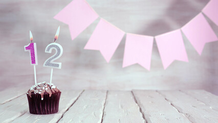 Birthday number 12. Festive background for a girl or woman with a muffin and candles burning pink...